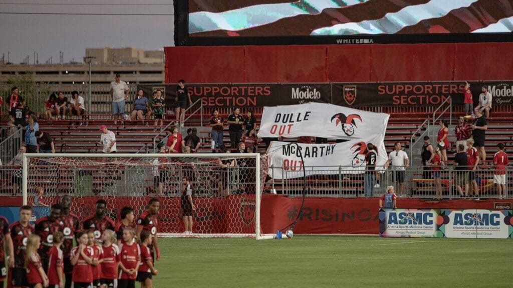Phoenix Rising supporters group Los Bandidos protests against Bobby Dulle and Brandon McCarthy by holding up white banners in the stands calling for both of them to go, accompanied by depictions of both wearing jester's hats and red noses.