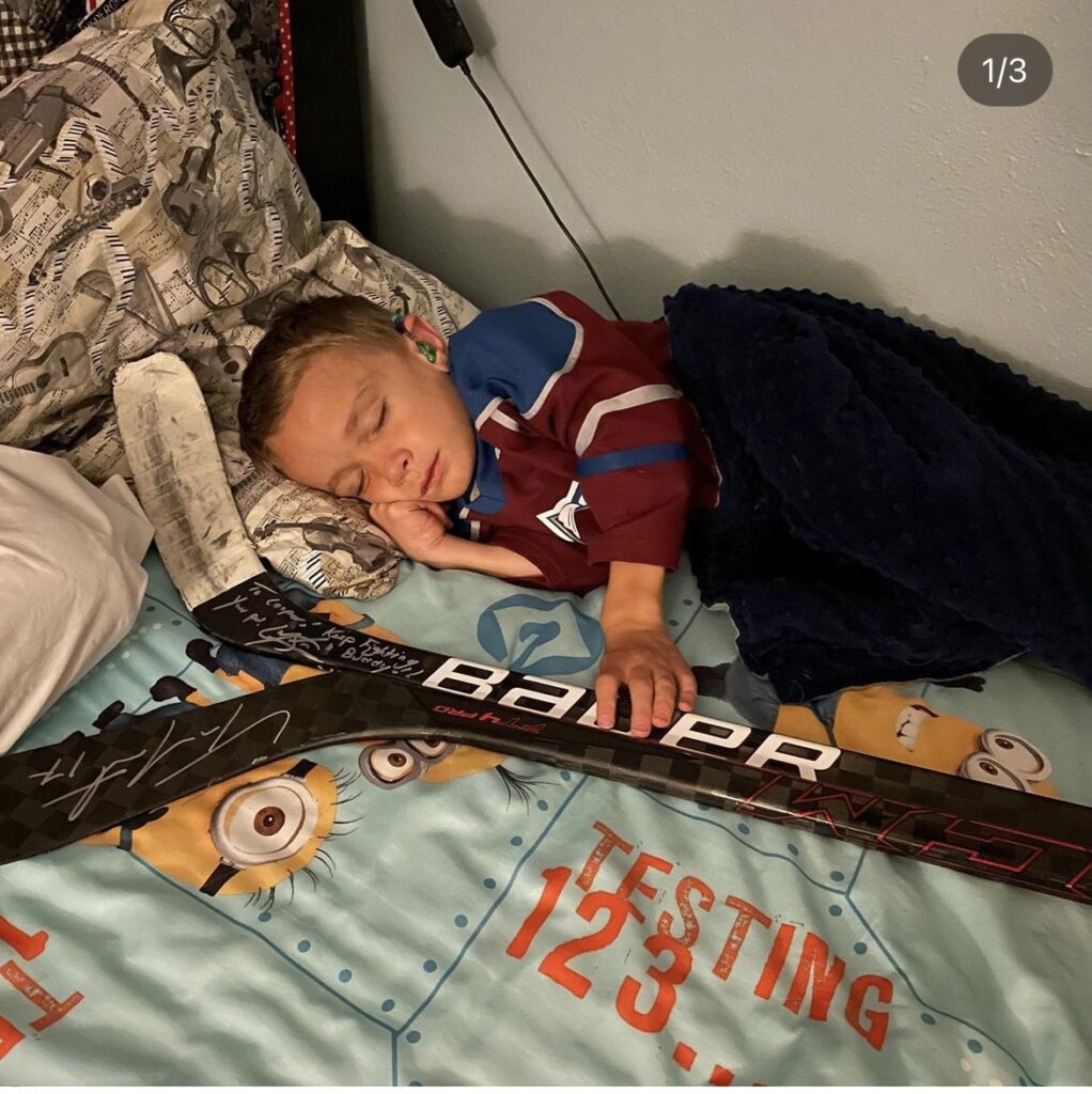 Cooper sleeping next to signed sticks from Cale Makar and Tyson Jost