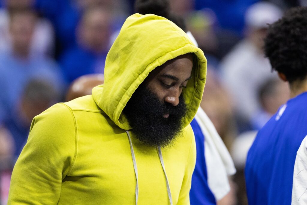 James Harden wearing a hoodie standing on the sidelines during a Sixers game.