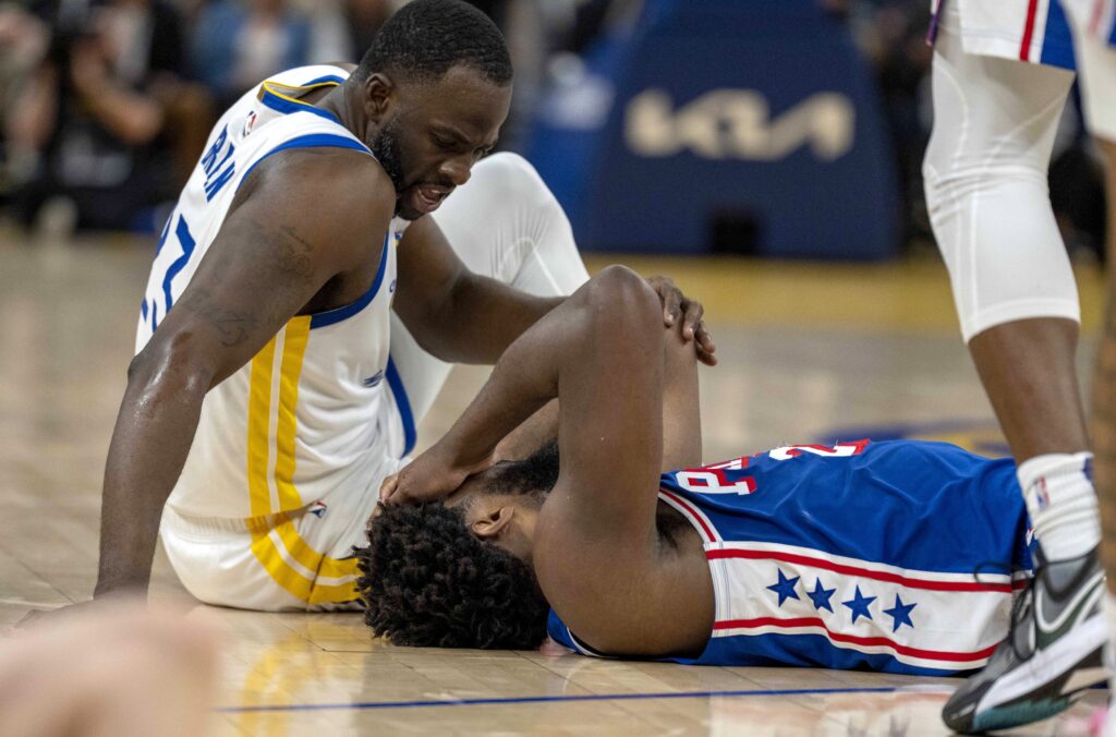 Joel Embiid laying on the floor next to Draymond Green.