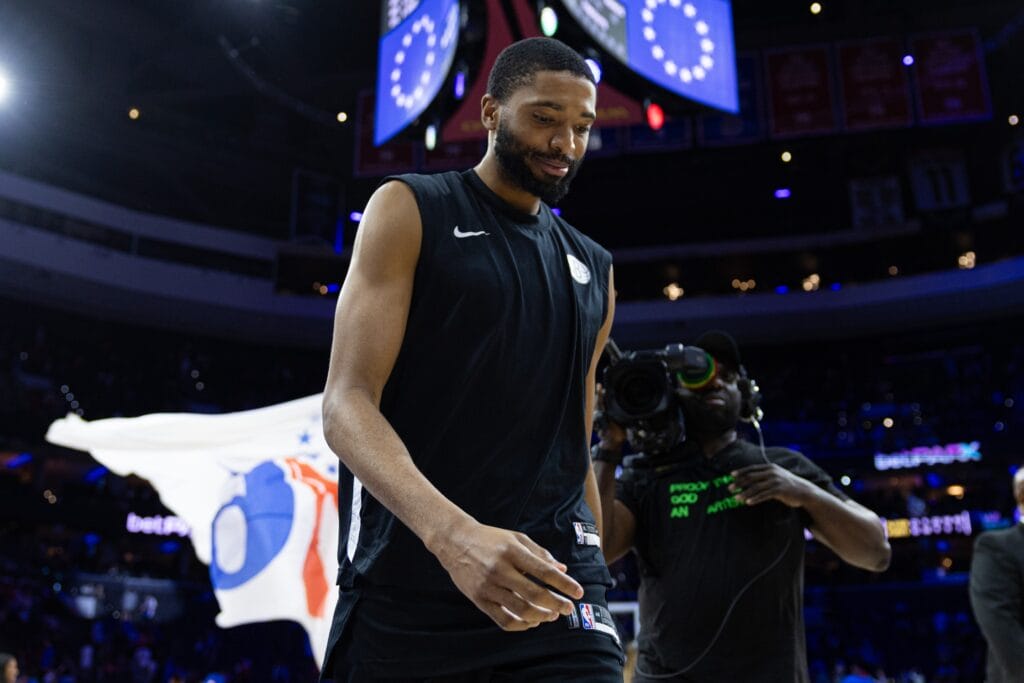 Mikal Bridges with a Sixers flag behind him.