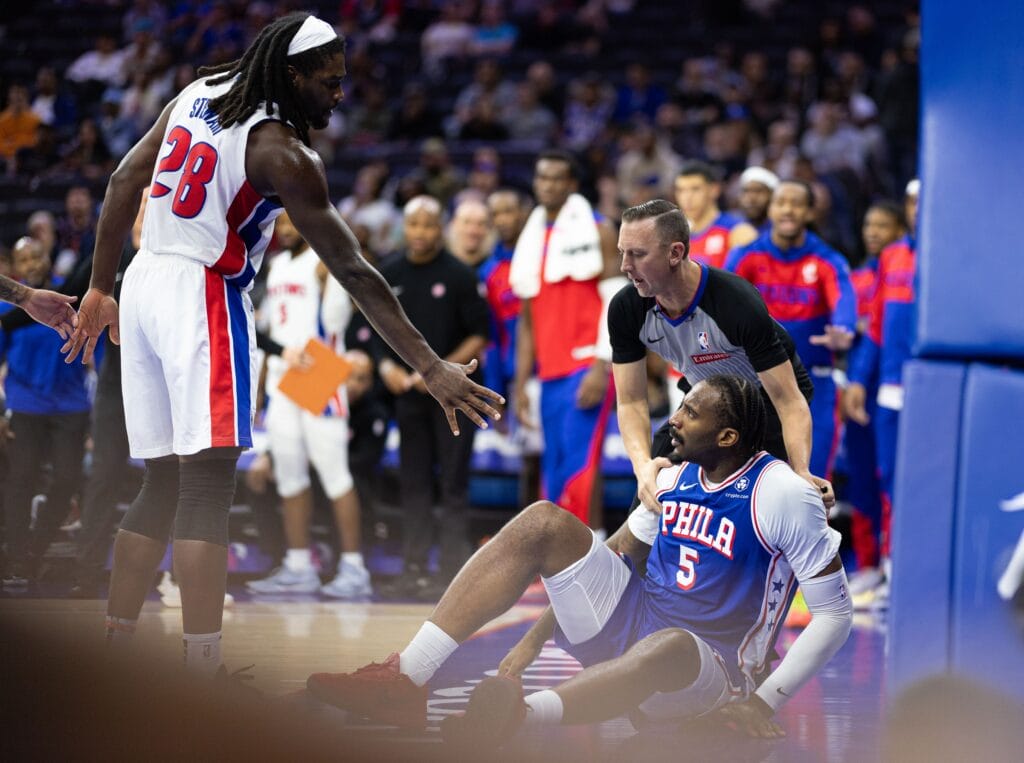 Andre Drummond sitting on the ground while being offered a handshake by