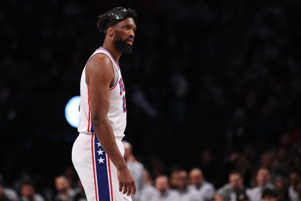 Joel Embiid standing midcourt with his mask on his head.