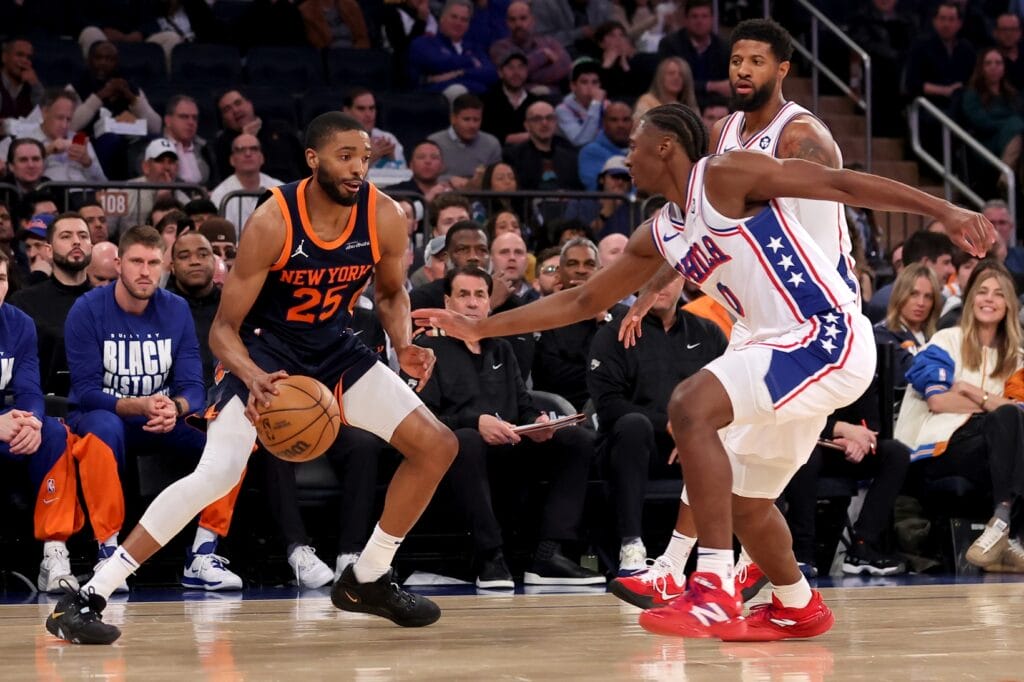Tyrese Maxey reaches at Mikal Bridges while he dribbles the ball.