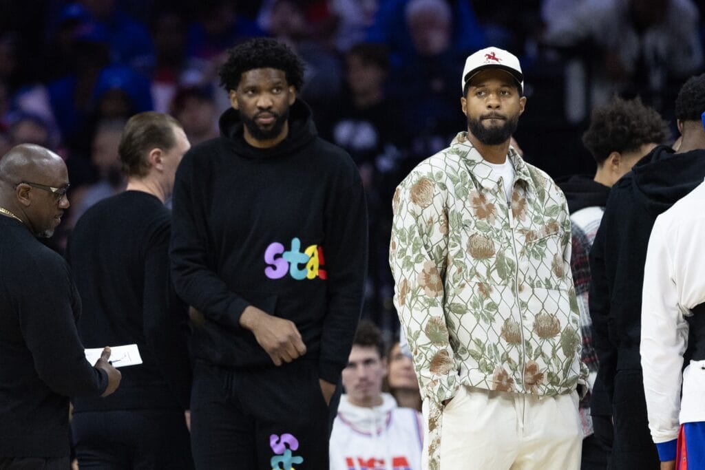 Paul George and Joel Embiid in street clothes at a Sixers game.